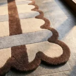 Close-up detail of the Linen Blend rug's corner, highlighting the plush hand-tufted wool texture, the intersecting lattice design, and the intricate brown scalloped border.