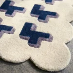 Close-up angled view of the Midnight Surge rug, highlighting the plush hand-tufted New Zealand wool and viscose silk texture, the deeply carved lines defining the 3D blue and lavender cross shapes, and the intricately contoured cream scalloped edge.
