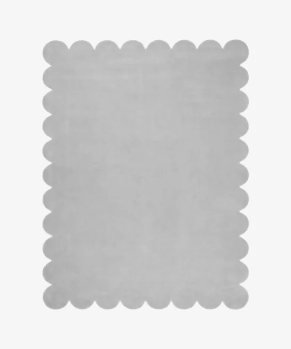 Top down flat lay of the Mistfall hand tufted rug featuring a calming solid silver gray color and decorative wavy edges isolated on a white background.
