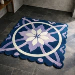 High angle view of the Moon Blossom square rug placed on a dark tiled floor, featuring a deep blue background with a striking central cream and lavender floral motif, a geometric white circular accent, and a decorative scalloped border.