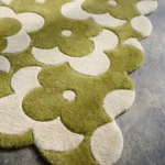 Close-up low angle view of the Moss Parade rug, showcasing the plush hand-tufted wool texture, the deeply carved lines defining the green and cream flower motifs, and the intricately contoured scalloped border.