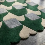 Close-up angled view of the Moss Rhythm rug, highlighting the dense, plush hand-tufted wool texture, the deeply carved lines defining the interlocking green and grey geometric shapes, and the intricately contoured scalloped edge.