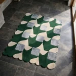 Perspective view of the Moss Rhythm rug placed on a dark tiled floor, showcasing the structured geometric checkerboard design and the organic green scalloped border illuminated by natural sunlight.