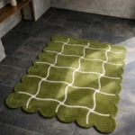 High angle view of the Moss Weave rug placed on a dark tiled floor, featuring an earthy moss green background with a contrasting cream wavy grid pattern, finished with a decorative scalloped edge.