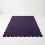 Low angle perspective of the Nightberry hand tufted rug placed on a white floor, highlighting the plush wool texture and the elegant wavy edge shape.
