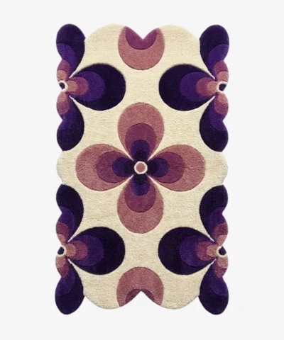 Top down flat lay of the Nocturne Bloom rug featuring a retro geometric floral pattern with dark purple and lilac petals on a cream wool background.