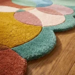 Close-up angled view of the Ochre Orbit runner rug placed on a warm wooden floor, highlighting the dense, plush hand-tufted New Zealand wool and viscose silk texture. The design features a playful geometric pattern of overlapping circles in an earthy yet vibrant palette of ochre yellow, muted teal, soft pink, terracotta, and light blue, which naturally form a dynamic, wavy contoured edge.