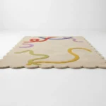 Angled perspective view of the Pastel Doodle hand tufted rug placed on a white floor showing the fun multicolor squiggle pattern and wavy border shape.
