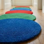 Close-up angled view of the Pastel Ring Stack runner rug on a wooden floor, highlighting the dense, plush hand-tufted New Zealand wool and viscose silk texture, the distinct intersection of the bright blue, green, and red circular blocks, and the gracefully contoured circular border.