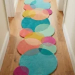 Perspective lifestyle view of the Pastel Tide runner rug placed on a warm wooden floor in a brightly lit hallway, featuring a playful geometric pattern of overlapping circles in vibrant pastel shades of teal, pink, yellow, orange, and magenta. The intersecting circular shapes naturally form a dynamic, wavy scalloped edge along the length of the hand-tufted New Zealand wool and viscose silk runner.