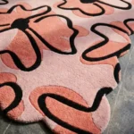 Close-up low angle view of the Peachy Sketch rug, showcasing the plush hand-tufted wool texture, the deeply carved thick black lines defining the abstract floral pattern, and the intricately wavy scalloped border.