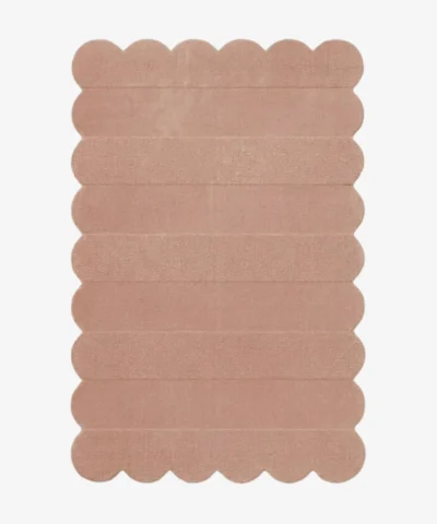 Top down view of the Petal Layers rug featuring a soft dusty pink color with horizontal carved textures and decorative scalloped edges.