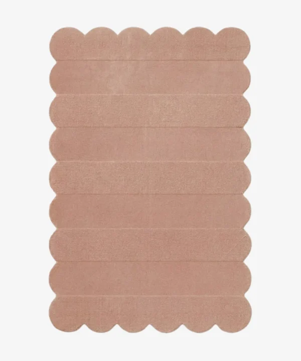 Top down view of the Petal Layers rug featuring a soft dusty pink color with horizontal carved textures and decorative scalloped edges.