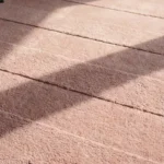 Close-up detail of the Petal Layers rug illuminated by sunlight, showcasing the dense hand-tufted wool texture, the deeply embossed horizontal lines, and the intricately carved pink scalloped border.