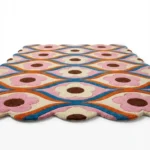 Angled perspective of the Petal Weave hand tufted rug showing the geometric flower design in vibrant pink orange and blue hues with scalloped edges.