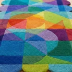 Close-up angled view of the Prism Cascade runner rug, highlighting the dense, plush hand-tufted New Zealand wool and viscose silk texture. The design features a vibrant, multi-colored mosaic of geometric shapes—including triangles, circles, and semi-circles—in a rainbow palette of blue, green, yellow, orange, purple, and red, which naturally form a playful, wavy scalloped edge.