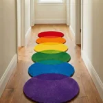 Perspective lifestyle view of the Rainbow Pulse runner rug placed on a warm wooden floor in a brightly lit hallway, showcasing the dynamic gradient of overlapping circles in vivid rainbow hues and the playful wavy scalloped silhouette extending down the corridor.
