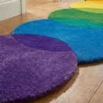 Close-up angled view of the Rainbow Pulse runner rug on a wooden floor, highlighting the dense, plush hand-tufted New Zealand wool and viscose silk texture, the distinct intersection of the purple, blue, and green circular blocks, and the gracefully contoured scalloped border.