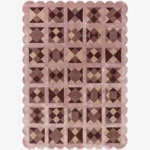 Top down view of the Rose Matrix rug against a white background, featuring a repeating patchwork pattern of geometric squares and diamonds in solid shades of soft pink, mauve, and deep burgundy, framed by a continuous pink scalloped border.