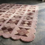 Close-up angled view of the Rose Matrix rug, highlighting the dense hand-tufted New Zealand wool texture, the deeply carved lines separating the geometric pink and burgundy patchwork shapes, and the intricately contoured scalloped edge.