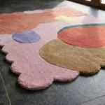 Close-up angled view of the Rose Riot rug, highlighting the dense hand-tufted New Zealand wool and viscose silk texture, the deeply carved lines separating the colorful organic abstract shapes, and the intricately contoured pink scalloped edge.