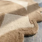 Close-up detail of the Rounded Dunes rug's border, highlighting the plush hand-tufted wool texture, the subtle contrast between the beige geometric shapes, and the intricately carved scalloped edge.