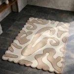 Perspective view of the Sand Drift rug placed on a dark tiled floor, showcasing the calming organic abstract design and the dynamically sculpted scalloped border illuminated by natural sunlight.