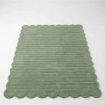 Angled view of the Sage Rhythm area rug showing the soft moss green wool and the rhythmic ribbed pattern on a white floor.