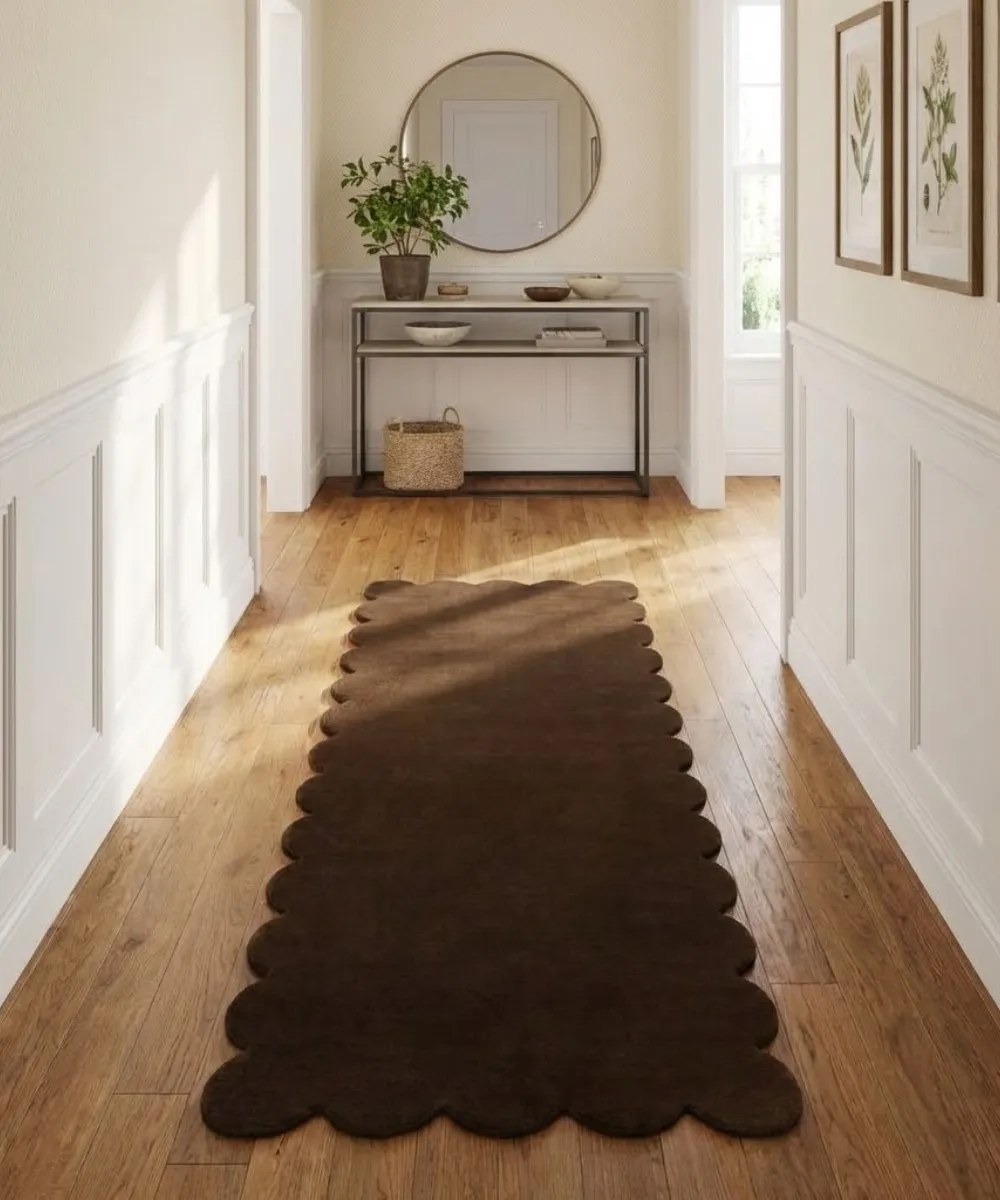 Lifestyle interior shot for the ScallopedRugs collection featuring a solid dark chocolate brown runner rug with custom wavy borders placed in a long hallway to add texture and warmth to the wooden flooring.