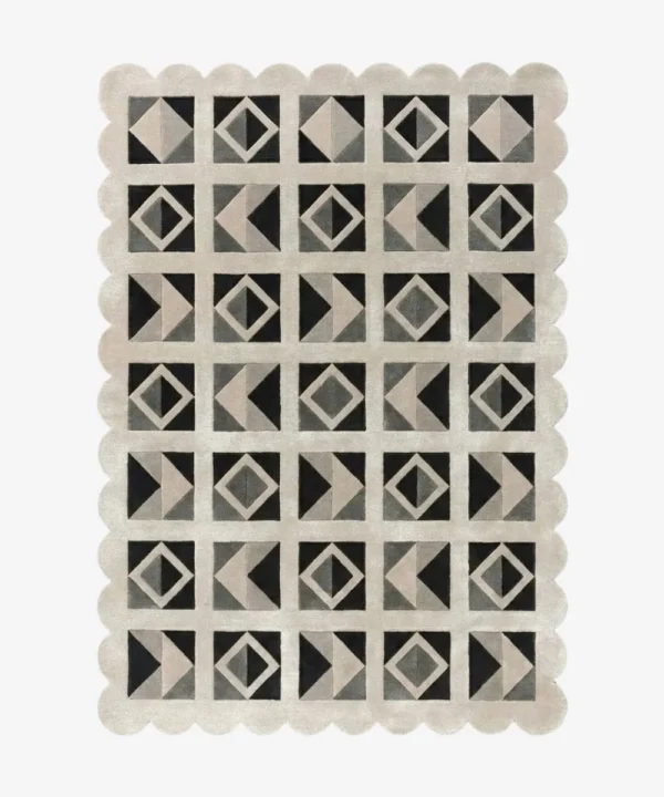 Top down view of the Shadow Grid rug against a white background, featuring a repeating patchwork pattern of geometric squares, triangles, and diamonds in shades of black, dark grey, light grey, and cream, framed by a continuous cream scalloped border.