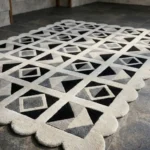Close-up angled view of the Shadow Grid rug, highlighting the dense hand-tufted wool texture, the deeply carved lines separating the geometric black, grey, and cream patchwork shapes, and the intricately contoured scalloped edge.