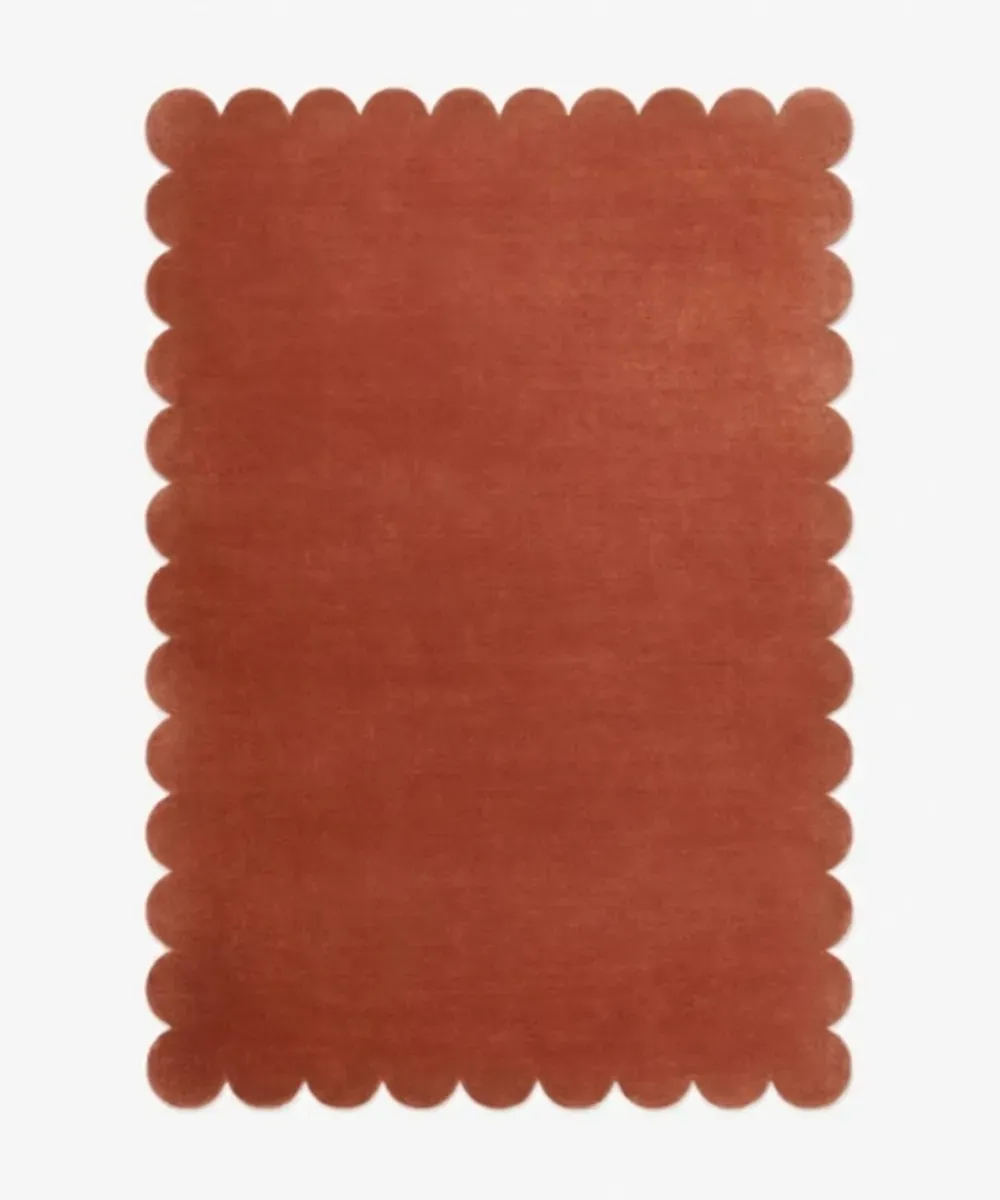A solid rust orange rug with decorative edges, serving as the button to explore the Solid and Monochromatic Rugs collection.