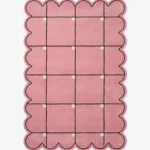 Top down view of the Soft Depth rug featuring a soft pink wool background with a delicate dark grid pattern accented by small white squares and custom scalloped edges.