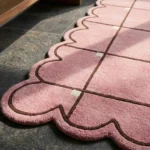 Close-up detail of the Soft Depth rug, highlighting the plush hand-tufted wool texture, the embossed dark brown grid lines with a cream accent square, and the intricate pink scalloped edge.