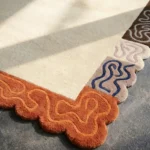 Close-up low angle view of the Soft Frame rug, highlighting the dense hand-tufted New Zealand wool texture, the solid cream center, and the deeply carved squiggly pattern within the colorful scalloped edge.