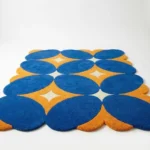 Angled shot of the Solar Indigo hand tufted rug placed on a white floor showcasing the decorative wavy scalloped borders and soft cut pile finish.