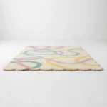 Low angle side view of the Sorbet Stream area rug placed on a white floor showing the plush pile height and the decorative wavy border shape.