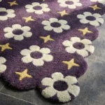 Close-up low angle view of the Starlit Bloom rug, showcasing the plush hand-tufted New Zealand wool texture, the deeply carved white flowers and yellow stars, and the intricately contoured purple scalloped border.