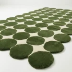Low angle close up shot of the Still Meadow rug highlighting the dense plush hand tufted wool pile and the crisp definition of the moss green circles.