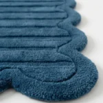 Close-up detail of the Still Tides rug, showcasing the dense hand-tufted wool texture, the deeply embossed horizontal lines, and the intricately carved blue scalloped border.