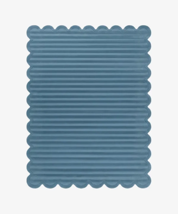 Top down view of the Still Tides rug featuring a solid dusty blue color with horizontal carved textures and decorative scalloped edges.