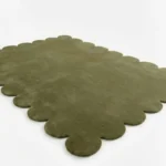 High angle perspective of the Stone Whisper hand tufted rug placed on a white floor, showing the rich moss green wool texture and the wavy edge design.