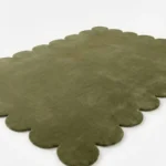 Low angle close up shot of the Stone Whisper area rug highlighting the dense plush pile and the precision of the hand cut scalloped shape in a deep green hue.