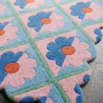 Close-up detail of the Sugar Trellis rug, highlighting the dense hand-tufted wool texture, the deeply carved mint green grid lines separating the two-tone pink and blue floral motifs, and the intricately contoured scalloped border.