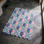 Perspective view of the Sugar Trellis rug placed on a dark tiled floor, featuring a mint green trellis grid filled with retro flowers split into pastel pink and blue halves, finished with a decorative scalloped edge.
