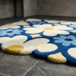 Close-up low angle view of the Sun Dot Posy rug, showcasing the plush hand-tufted wool texture, the deeply carved lines separating the bold cream, yellow, and blue floral motifs, and the intricately contoured scalloped border.