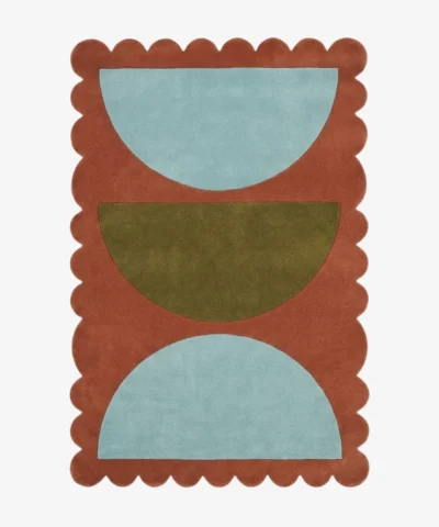 Top down view of the Sunbaked Form rug featuring a bold geometric pattern with large light blue and olive green semi-circles on a terracotta rust wool background with scalloped edges.