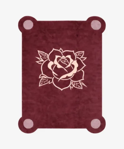 Top down view of the Velvet Bloom rug featuring a deep maroon wool background with a central traditional tattoo-style rose illustration in light pink and cream, framed by decorative pink corner accents.