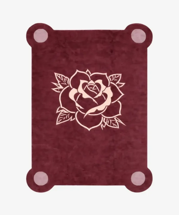 Top down view of the Velvet Bloom rug featuring a deep maroon wool background with a central traditional tattoo-style rose illustration in light pink and cream, framed by decorative pink corner accents.