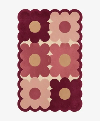 Top down view of the Velvet Garden rug featuring a playful grid pattern of large maroon and dusty pink flowers on a cream wool background, finished with custom scalloped edges.